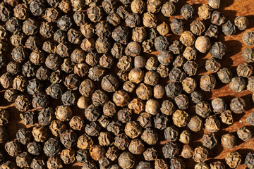 Whole black peppercorns scattered across a tabletop in the afternoon sun.