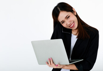 Asian beautiful business woman wearing formal black suit, smiling with happiness, typing and using laptop for working while talking or communicating on mobile phone with isolated white background.