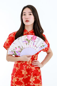 A Chinese beautiful woman with long black hairs in red traditional dress is standing and holding native style paper fan in front of herself.