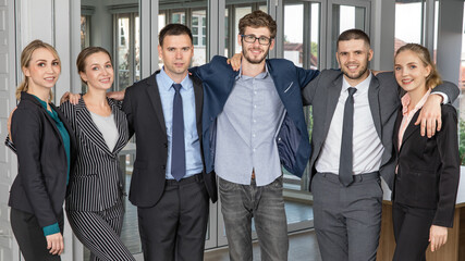 Group portrait of six business people team standing together in an office and cuddle around necks together with smile faces and self-confidence. Idea for success of teamwork in modern business