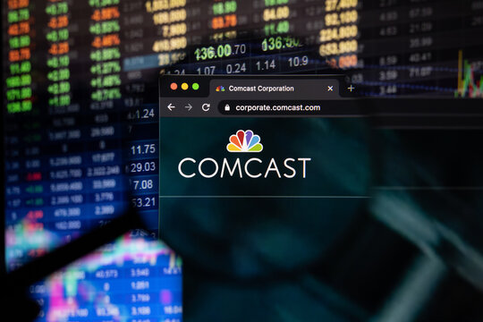 Comcast company logo on a website with blurry stock market developments in the background, seen on a computer screen through a magnifying glass