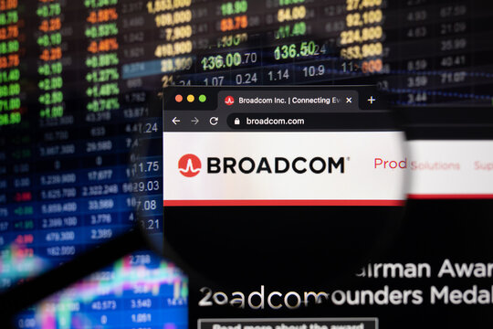 Broadcom company logo on a website with blurry stock market developments in the background, seen on a computer screen through a magnifying glass