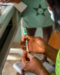 closeup of a black descent hand holding vaccine bottle and syringe