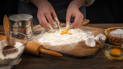 Women's hands, flour and dough. A woman in an apron prepares dough for homemade baking, a rustic home cozy atmosphere, a dark background with unusual lighting.