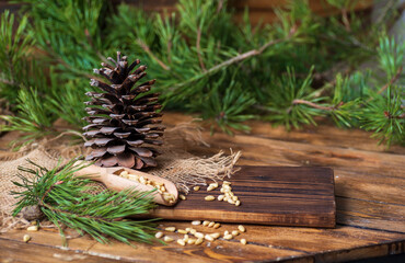 Pine cone on a board with pine nuts. Pine branches with green needles lie around on the table. 