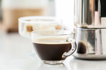 Coffee maker and cup of espresso on table in kitchen