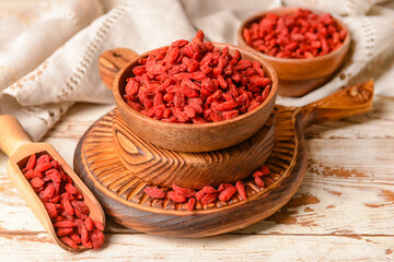 Bowl and scoop with dried goji berries on light wooden background