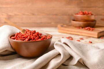 Bowl with dried goji berries on light wooden background