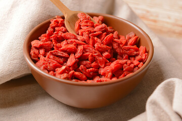 Bowl with dried goji berries on light wooden background