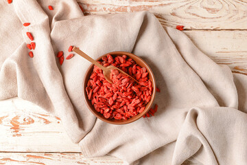 Bowl and scoop with dried goji berries on light wooden background