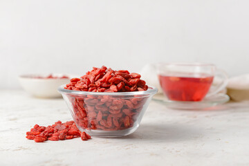 Bowl with dried goji berries on light background