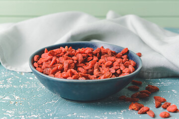 Bowl with dried goji berries on color background