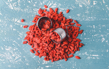 Infuser with dried goji berries on color background