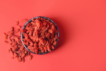 Bowl with dried goji berries on color background