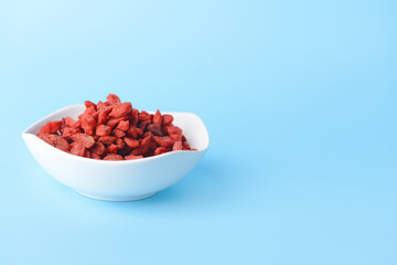 Bowl with dried goji berries on color background