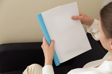 Beautiful female hands hold an open book or magazine in a room on a black sofa