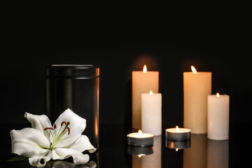 Lily flower with mortuary urn and candles on dark background