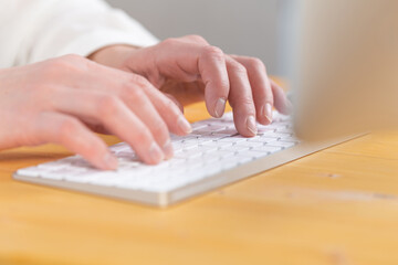 Fototapeta na wymiar An image of a woman's hand is typing on a white keyboard on a wooden table. Selective focus