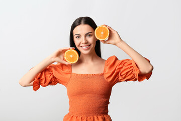 Beautiful young woman with orange on light background