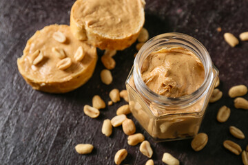 Jar and bread with tasty peanut butter on dark background