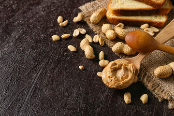 Spoon and toast with tasty peanut butter on dark background