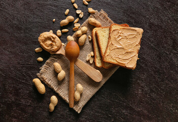 Spoon and toast with tasty peanut butter on dark background