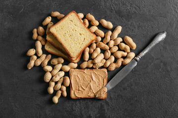 Toast with tasty peanut butter and nuts on dark background