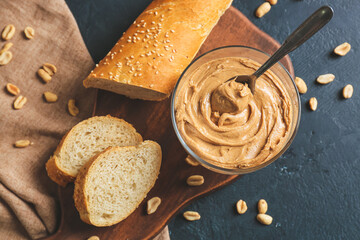 Glass bowl with tasty peanut butter and bread on dark background