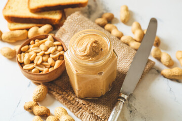 Jar with tasty peanut butter and nuts on light background