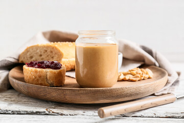 Jar with tasty peanut butter, bread and jam on light wooden background
