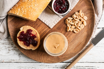 Jar with tasty peanut butter, bread and jam on light wooden background