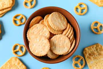 Bowl with tasty different crackers on color background