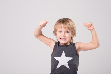 Caucasian child in a black and white T-shirt with star made gesture with his hands, showing super power, muscle. Portrait of cheerful boy. Childhood, growing up, kid's health concept. Copy space.