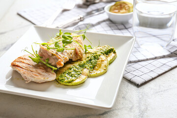 Plate with tasty grilled chicken meat, zucchini and pesto sauce on light background, closeup