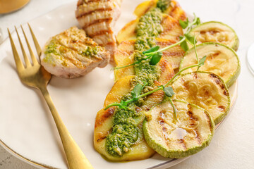 Plate with tasty grilled chicken, vegetables and pesto sauce on light background, closeup
