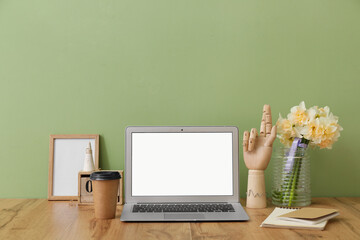 Stylish workplace with laptop and beautiful daffodils near color wall