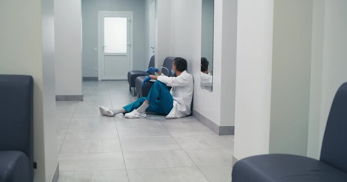Stressed middle aged doctor resting in clinic hallway during pandemic
