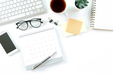 Modern white office desk table with computer, calendar, notebook, tree, glasses and cup of coffee. Top view with copy space,