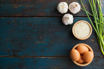 Multiple eggs in a cup with garlic and onions lay on a vintage wooden floor.