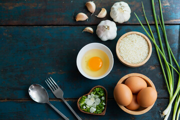 Multiple eggs in a cup with garlic and onions lay on a vintage wooden floor.