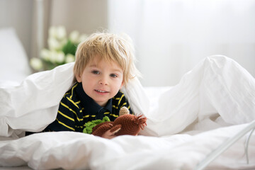 Fototapeta premium Blond toddler child in bed with stuffed monkey, playing in the morning