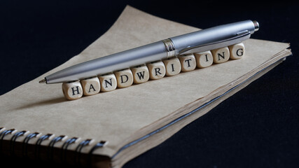 A shiny metal fountain pen rests on a notebook made of eco-friendly paper and the inscriptions are handwriting. Handwriting and calligraphy concept