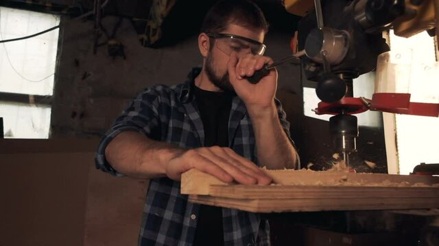 Handyman drilling wood plank at workshop with machine
