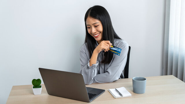 Young asian woman holding credit card and looking on laptop to using for online shopping