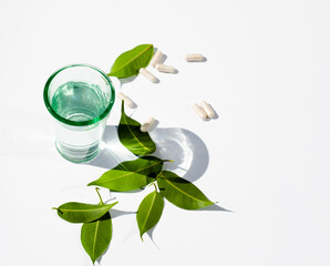 Glass of water. Capsules. Pills. Green leaves. White background. Copy space for text. Alternative medicine topics.