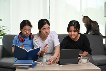 Three children watching cartoons online on digital tablet and sitting on sofa together.