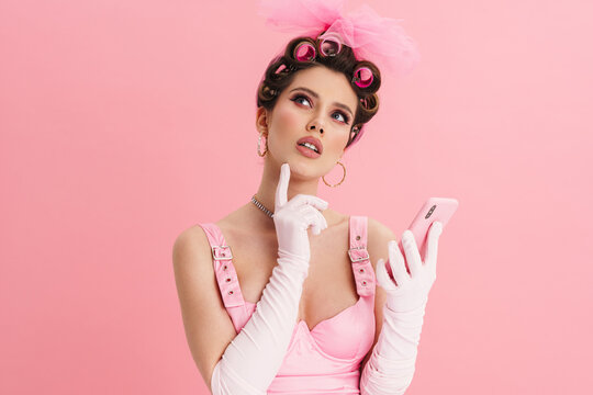 Puzzled woman with curlers looking upward and using cellphone