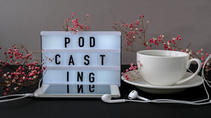 Podcasting lettering. Headphones mobile phone. Dry pink flowers decoration. Workplace. Black coffee