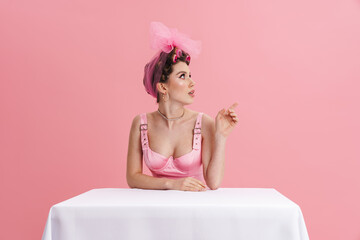 Young woman wearing curlers pointing finger aside while sitting at table