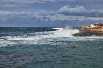 Fototapeta premium Water spraying in the air as waves crash against a rock on a beach in Qawra, Malta.
